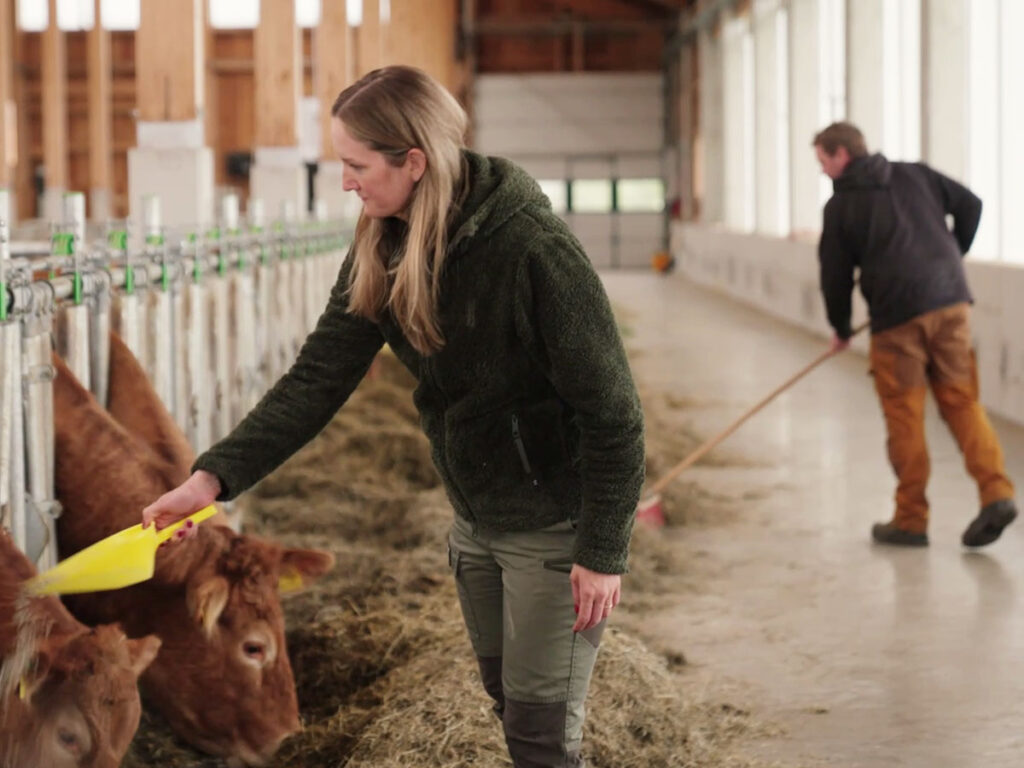 Stefanie und Florian Reinbacher bei der Stallarbeit im neuen Stall mit Fokus auf Tierwohl, Tageslicht und natürliche Belüftung.